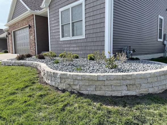 Curved stone bed with river rock and new shrubs along a home foundation